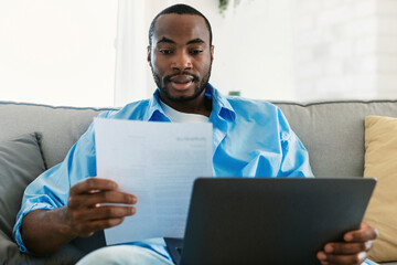 Remote career, freelance job concept. Young african american man using laptop computer and looking through documents