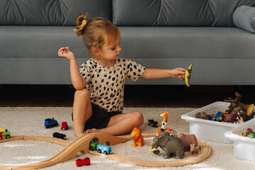 Kid girl builds a toy town and  wooden railway. A little girl sitting on floor plays with toy train...