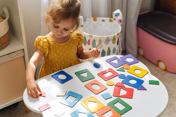 A little girl playing with wooden shape sorter toy on the table in playroom. Educational boards for...