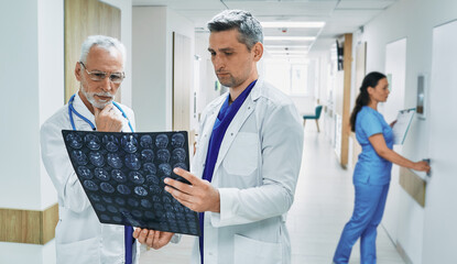 Obraz premium Two doctors analyzing MRI scan of patient's brain while standing in corridor of modern clinic during working day. Medical teamwork