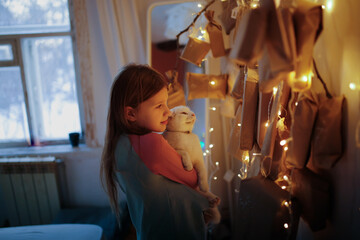 Magic photo. child with white cat and an advent calendar in eco-rust paper and garland lights.