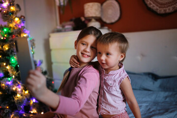 Obraz premium Cute sibling children in pajamas on bed in bedroom with smartphone, christmas, dark style.