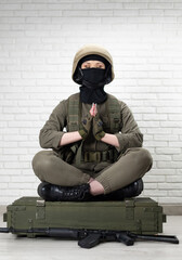 a girl soldier in a helmet sits in the lotus position on a box of ammunition