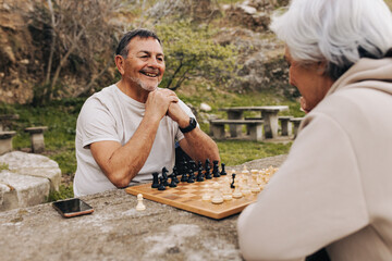 Carefree elderly couple enjoying a game of chess in a park