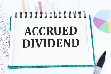 accrued DIVIDEND on a sheet of notepad on the table against the background of reports and charts, there is a black marker next to it
