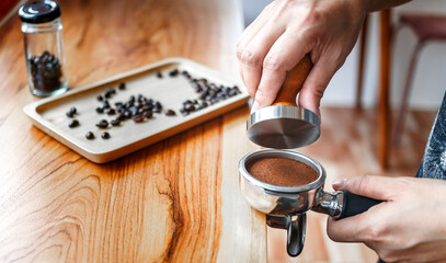 Barista cafe making coffee with manual presses ground coffee using tamper on the wooden counter bar at the coffee shop