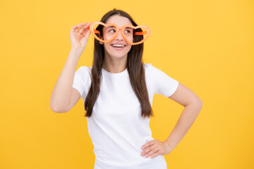 Beauty funny teenage girl with party glasses, yellow background. Surprised young woman with heart shaped glasses.
