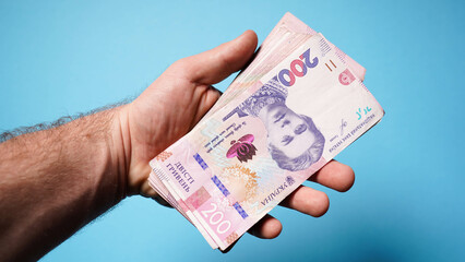 Male hand holds Ukrainian banknotes on a blue background