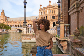 Naklejka premium beautiful woman with curly hair is on holiday in sevilla. The woman is posing for pictures in front of the most famous square of the centuries old city. Holiday and travel concept.