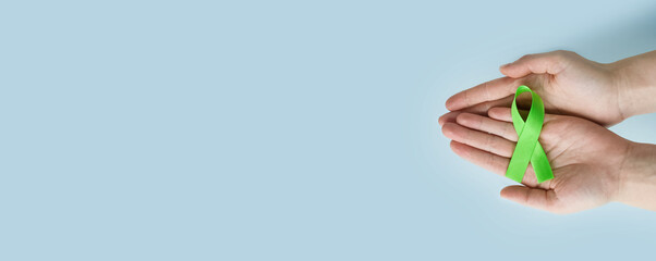 World Mental health awareness day. Woman hands holding green ribbon on blue background.