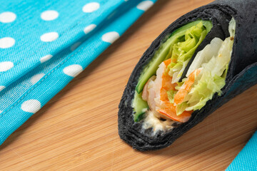 Tortilla wrap with shrimps and vegetables on wooden background