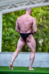 White man on stage with green grass demonstrates a beautiful male body with tensed muscles