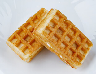 Delicious fresh Viennese waffles with white cream lie on a white plate.