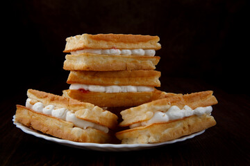 Four fresh Viennese waffles with white cream lie on a white plate.