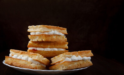 Four fresh Viennese waffles with white cream lie on a white plate.