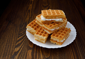 A pile of ruddy Viennese waffles lie on a white plate on a wooden background.
