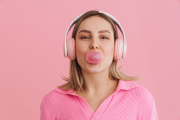 Young cute girl in pink headphones blowing bubble gum