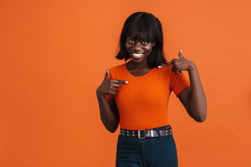 Fototapeta na wymiar Happy black woman pointing fingers at herself over orange background