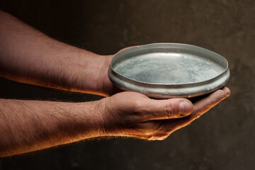 Male hands holding empty plate on dark background, lack of food, hunger concept.