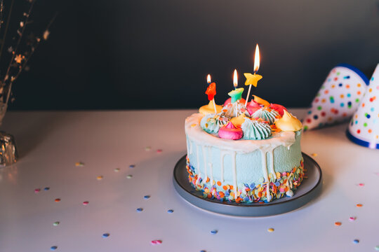 Colorful birthday cake with sprinkles and burning star shaped candles on a dark wall background. Festive birthday celebration, party. Selective focus, copy space.