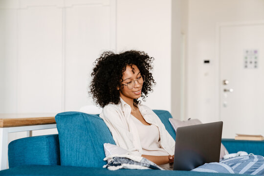 Black woman working with laptop while resting on couch at home