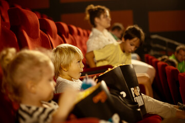 Cute child, curly girl, watching movie in a cinema, eating popcorn and enjoying