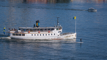 A steam commuting boat leaving for the archipelago and an electric motor surfboard passing in the bay Saltsjön a sunny autumn day in Stockholm