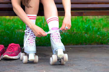 Female skater binds the roller skates on the bench in a park - obrazy, fototapety, plakaty