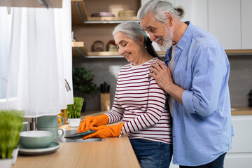 Portrait Of Happy Senior Spouses Washing Dishes In Kitchen After Lunch