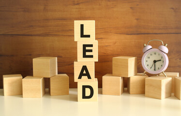 Four wooden cubes stacked vertically on a brown background form the word LEAD.