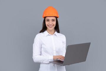 Young woman in hard hat helmet with laptop computer isolated on grey background. Architect woman wear helmet and shirt. Business woman, construction manager, builder.