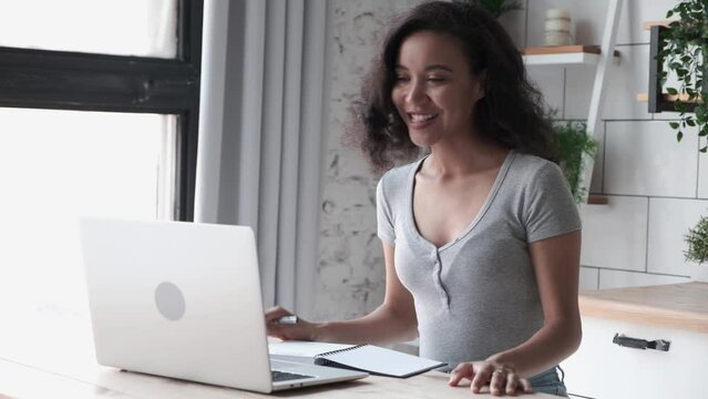 Happy lifestyle online digital job people working with laptop computer at home office, smilling freelance woman use pc on the desktop, takes notes. African american female technology occupation life