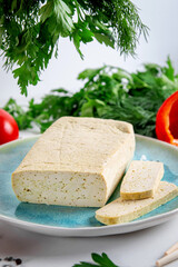 Sliced tofu soy cheese on a cutting board with basil, spices and vegetables