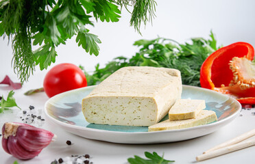 Sliced tofu soy cheese on a cutting board with basil, spices and vegetables