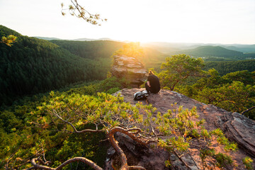 Mädchen sitzt zum Sonnenuntergang auf einem Felsen im Pfälzerwald in Rheinland Pfalz in Deutschland