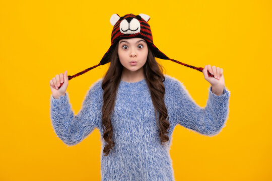 Modern teen girl wearing sweater and knitted hat on isolated yellow background. Funny face.