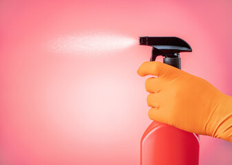 Hand in glove holds a spray of cleaning fluid on a pink background with copy space. Cleaning service concept.