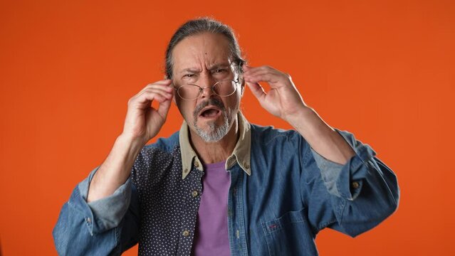 Old man struggles to hear, having difficulty hearing, isolated on solid orange background studio portrait.