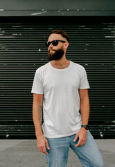 Young bearded hipster guy wearing white blank t-shirt and blue jeans in a random urban style. Design men t shirt mock-up for print