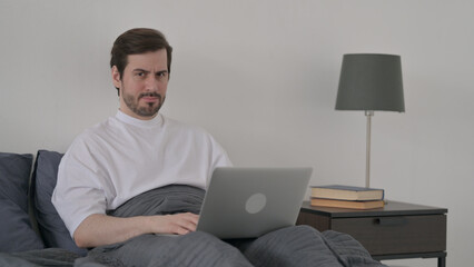 Young Man with Laptop Saying No by Head Shake in Bed