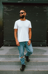 Young bearded hipster guy wearing white blank t-shirt and blue jeans in a random urban style....