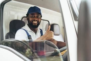 Portrait of courier black man in the truck thumb up and smiling to camera while sitting in driver seat, Optimistic man worker with delivery occupation. - obrazy, fototapety, plakaty