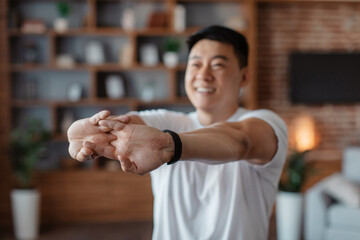 Fototapeta na wymiar Happy korean mature man stretching arms before domestic training, warming up his hands during home workout