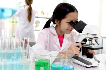 Adorable schoolgirl in lab coat doing science experiments, young scientist looking through...