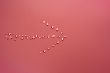 Arrow from drops of pure water, on a pink background. Sign showing the way. Copy space. Top view. 