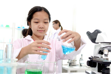 Adorable Asian schoolgirl in lab coat doing science experiments, pouring blue reagent solution from...