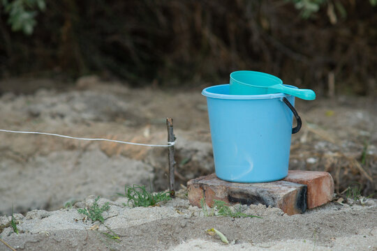 A Blue Plastic Dipper And A Bucket Stand On Bricks