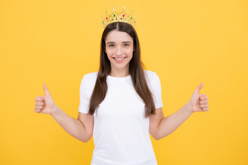Portrait of ambitious girl with crown, feeling princess, confidence. Studio shot isolated on yellow...