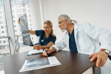 Obraz premium Team of doctors looking on results of X-Ray or MRI scan of patient's spine in medicine office