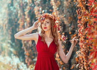 Autumn beauty. Portrait of a girl with beautiful curly red hair in a red dress posing in a wreath of flowers and grape leaves on a natural background. Autumn colors.